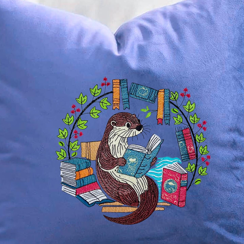 Almohada azul con un diseño bordado de una nutria leyendo libros.
