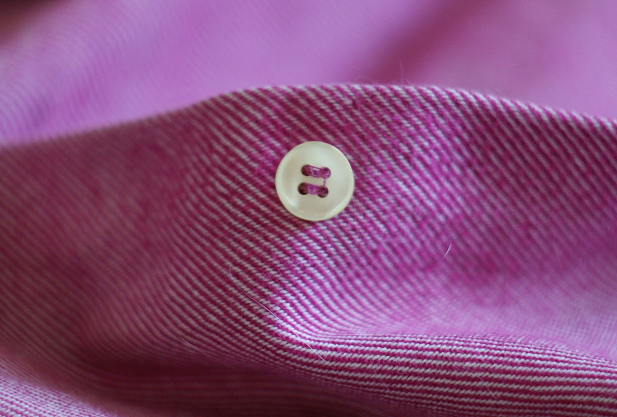 Close-up of a white button on a pink shirt.