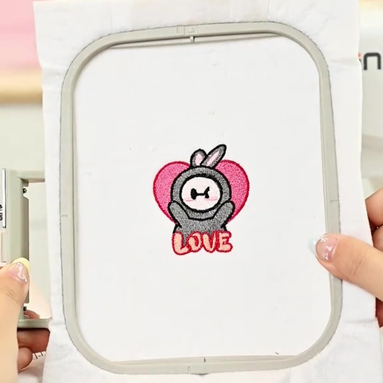 Hand holding an embroidery hoop with an embroidered design of the PooLin mascot and the word LOVE.