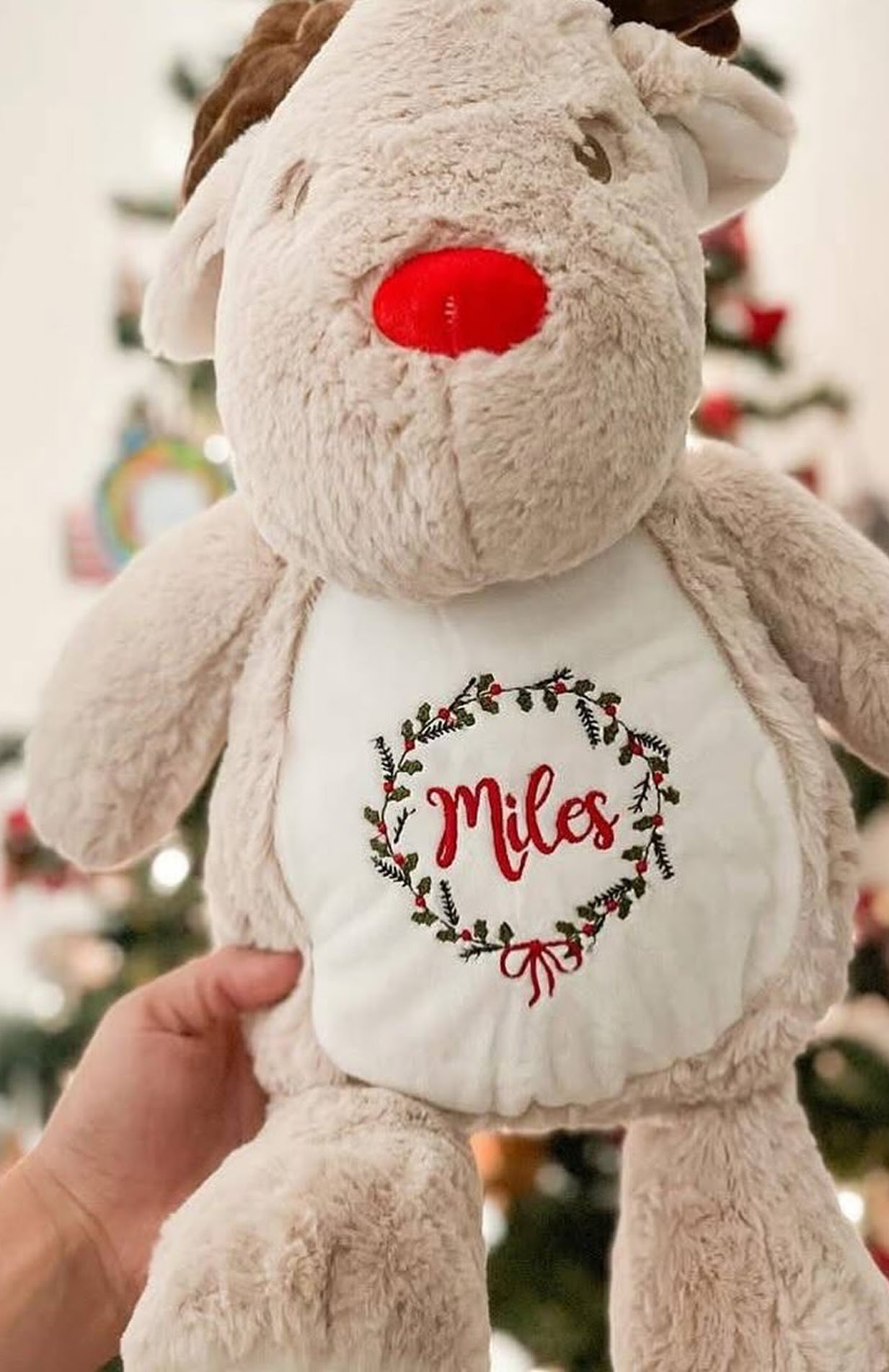Reindeer plushie with an embroidered design of a Christmas wreath and the name Miles in its belly.