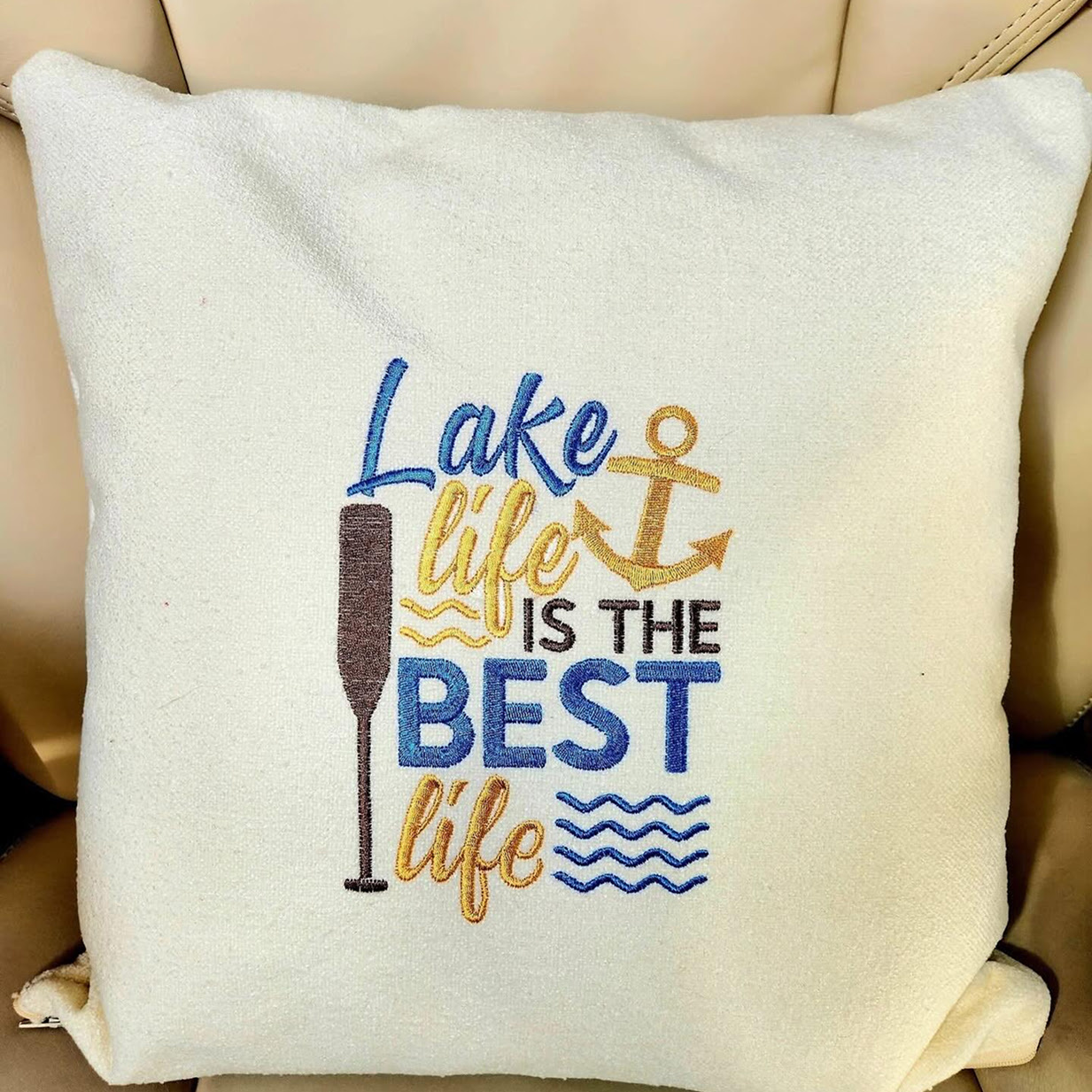 White pillow with an embroidered design of the text: Lake life is the BEST life, with an anchor and paddle.