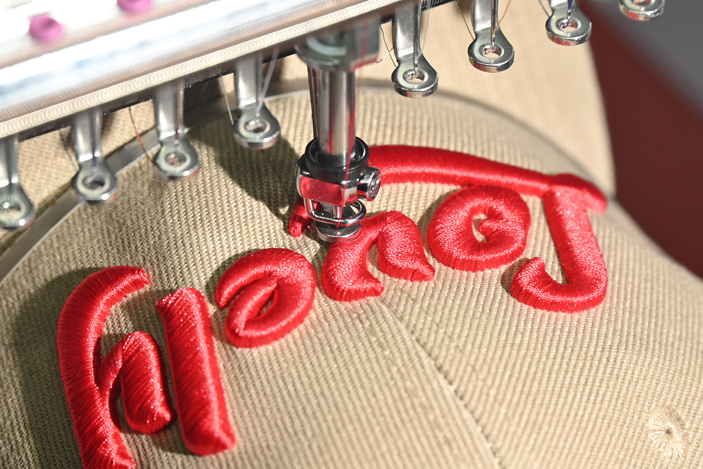 PooLin EOM embroidering the text Lovely in red on a beige cap.