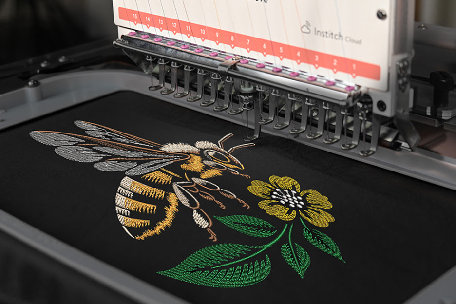 Close-up of the PooLin EOM embroidering a honey bee and flower on a black shirt