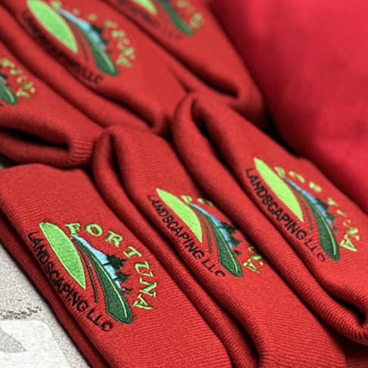 Several red beanies with an embroidered logo for a landscaping company.