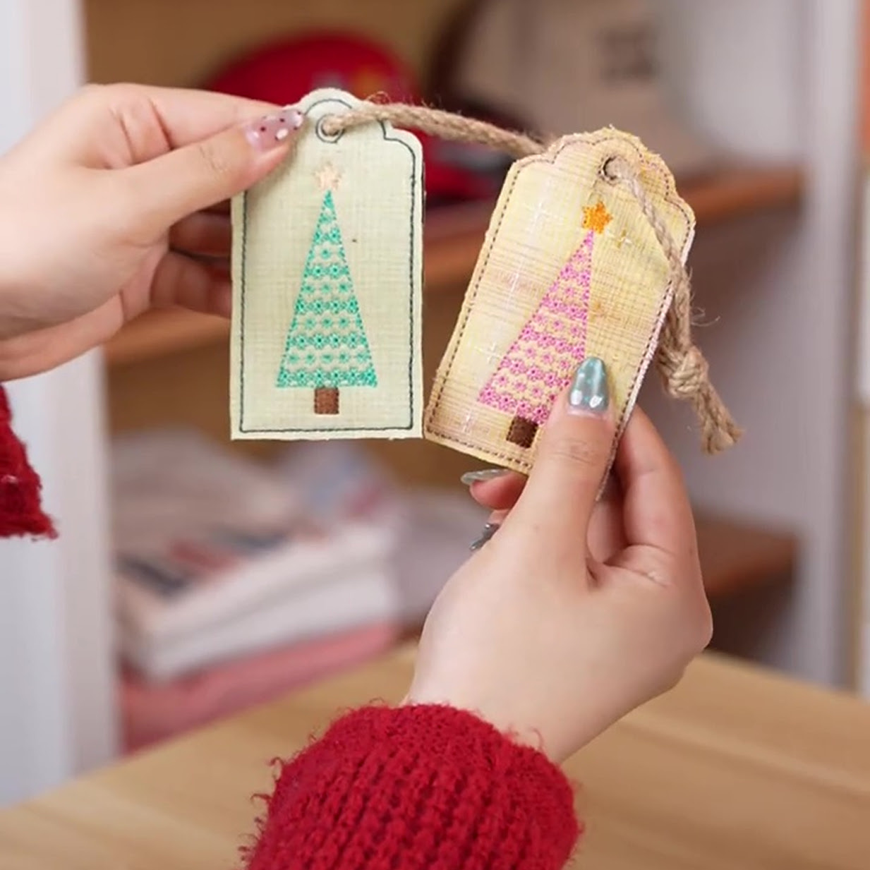 Hand holding two fabric labels with an embroidered design of a Christmas tree.
