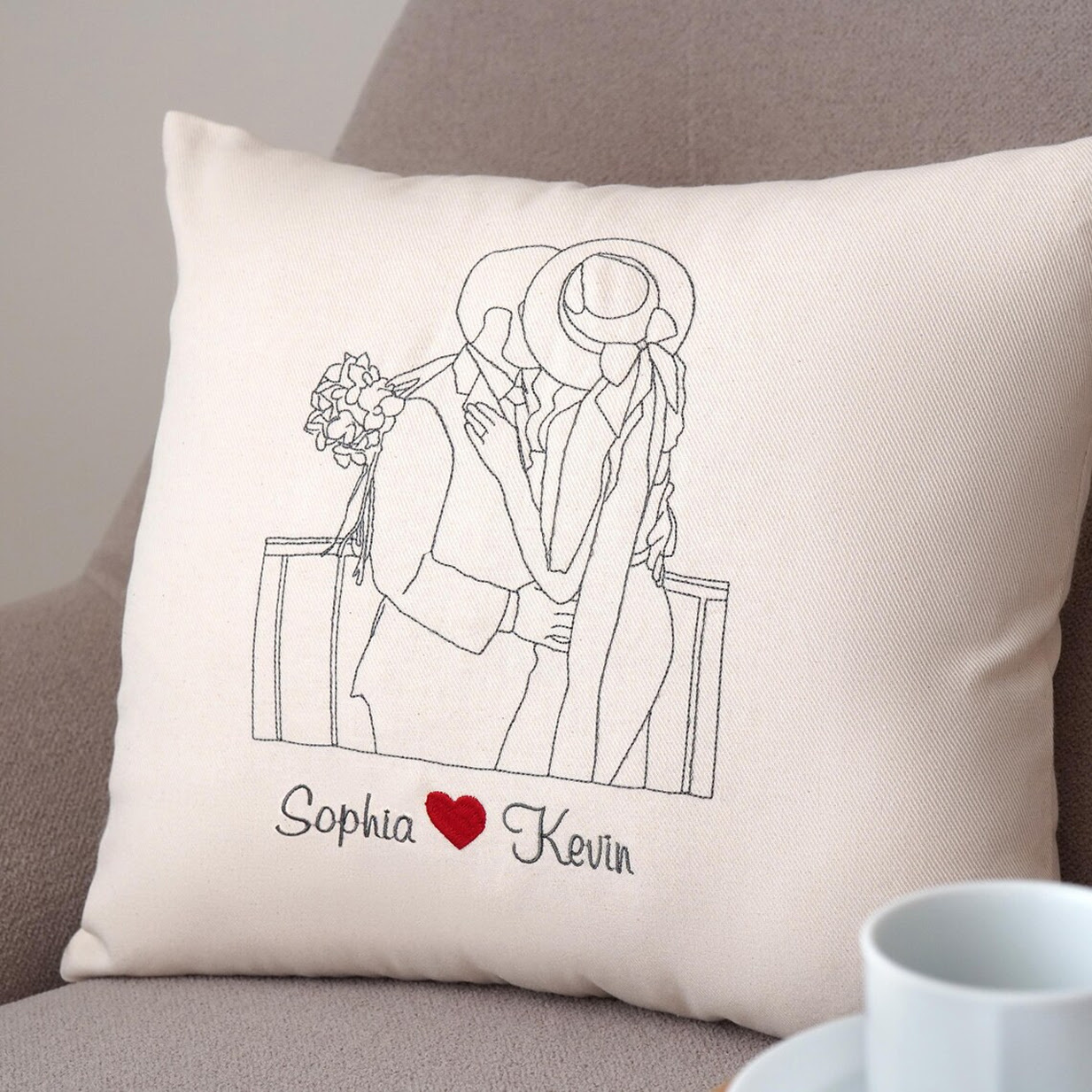 Custom embroidered throw pillow featuring a minimalist line-art portrait of a wedding couple kissing, personalised with the names Sophia and Kevin separated by a red heart.