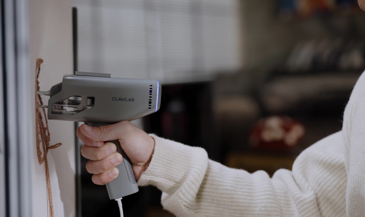 Hand holding the Clawlab Tufting Gun H1 while tufting with brown yarn.
