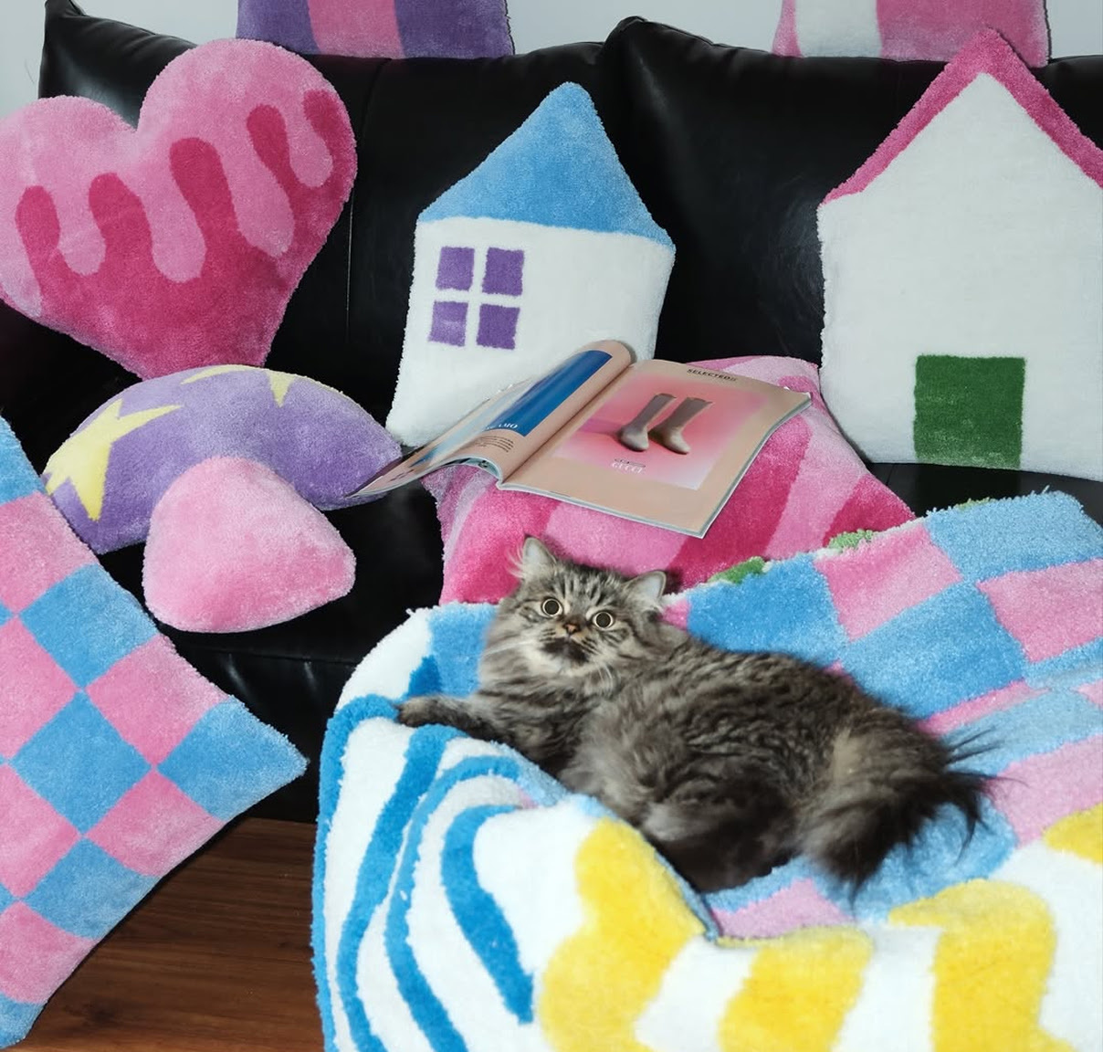 Cat lying on a tufted pillow surrounded by tufted home décor in pink, blue white and purple.
