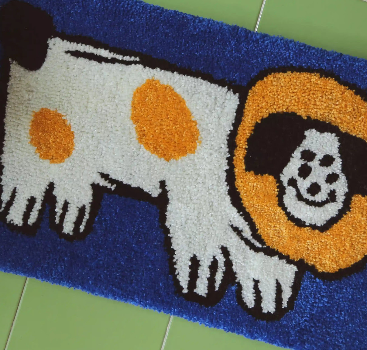 Tufted rug of a cartoon dog with  blue, yellow and white yarn.