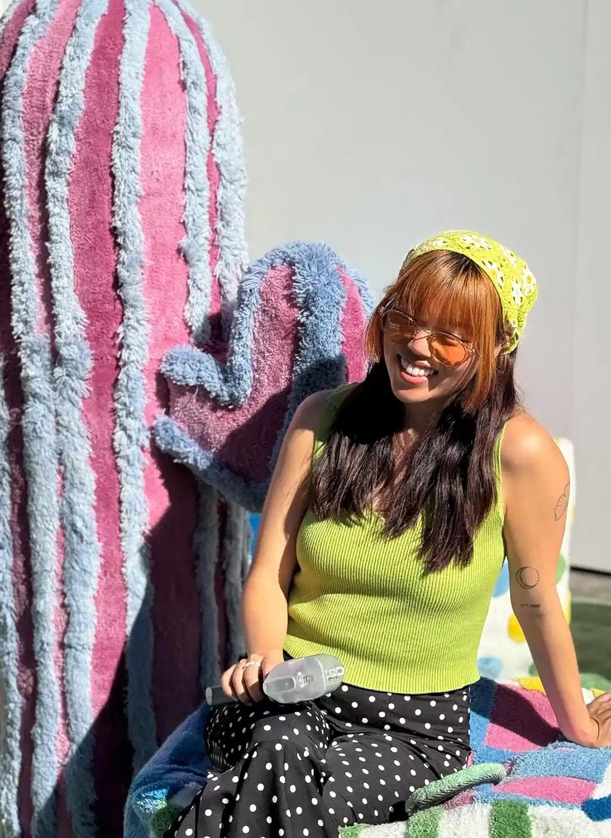 Smiling woman in front of a large pink and blue tufted and stuffed cactus
