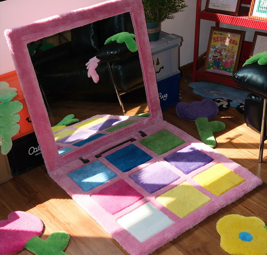Tufted rug of a pink make-up palette with shades of blue, puprle, pink, green and white and a large mirror. 