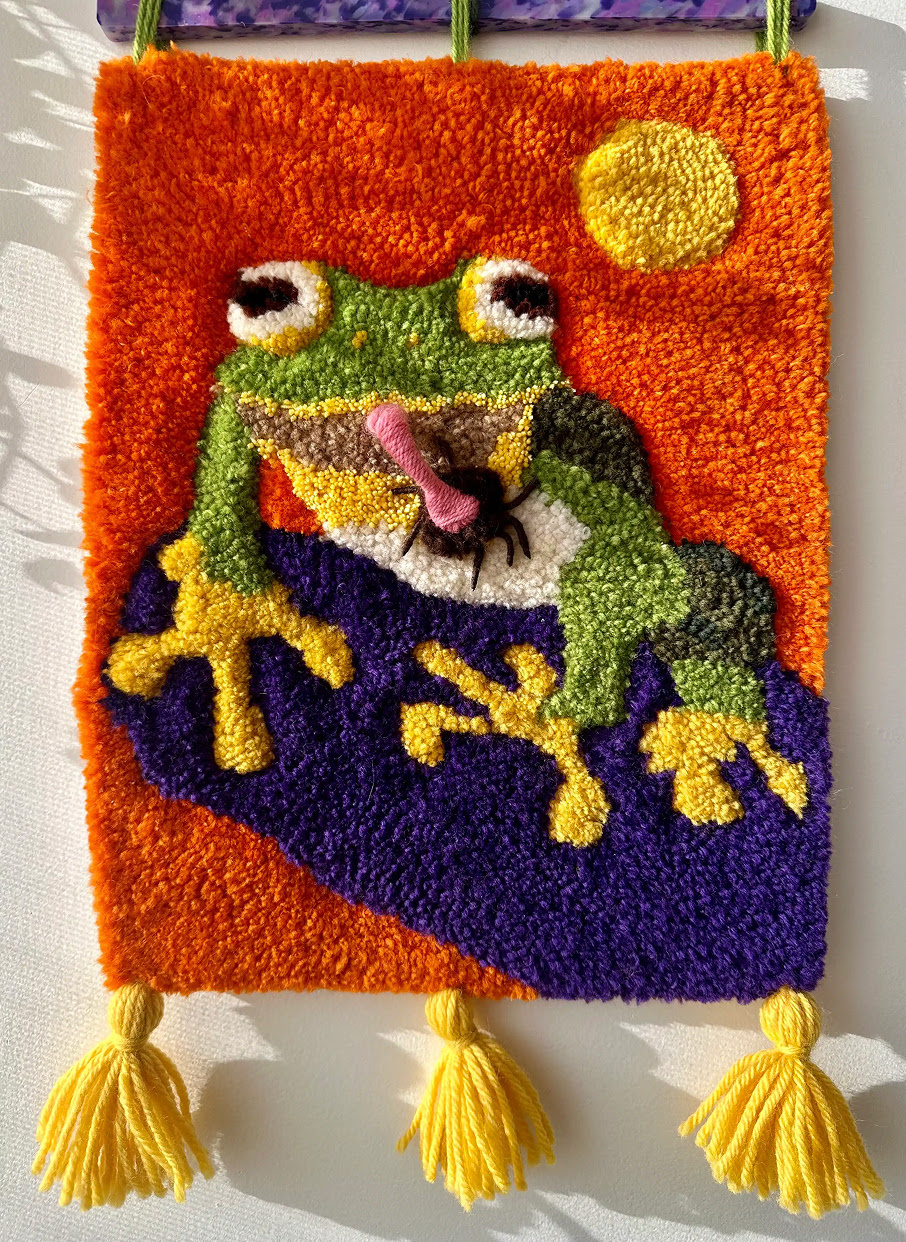 Tufted rug of a green frog against an orange background.