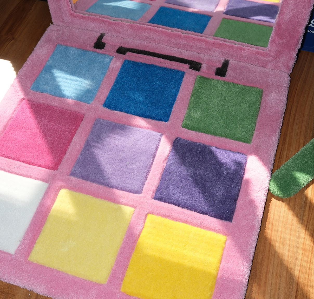 Tufted rug of a pink make-up palette with shades of blue, puprle, pink, green and white and a large mirror.