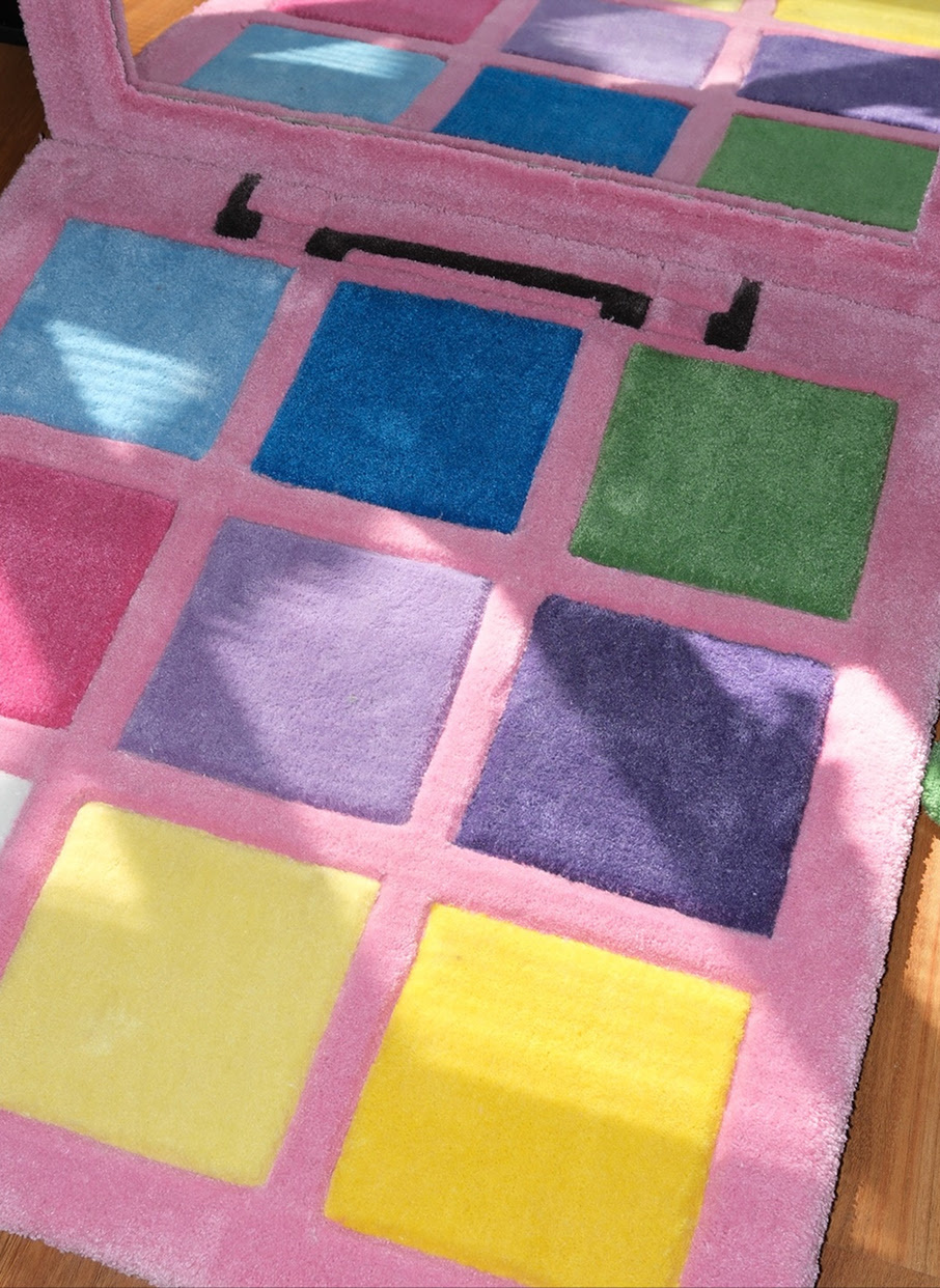 Tufted rug of a pink make-up palette with shades of blue, puprle, pink, green and white and a large mirror.
