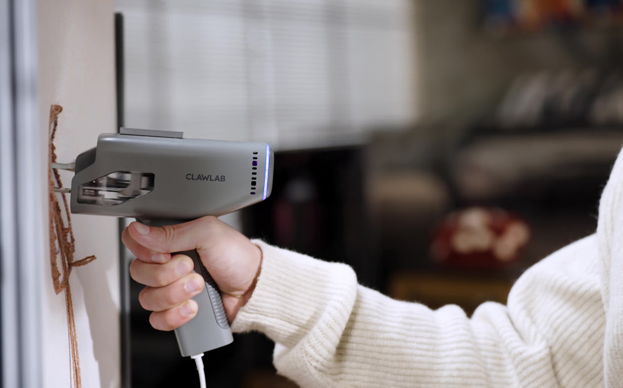 Hand holding the Clawlab Tufting Gun H1, tufting with brown yarn. 
