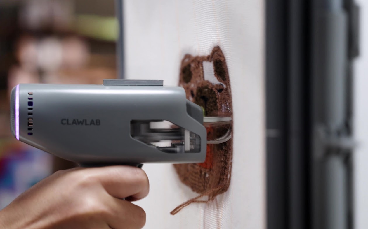 Hand holding the Clawlab Tufting Gun H1, tufting with brown yarn.