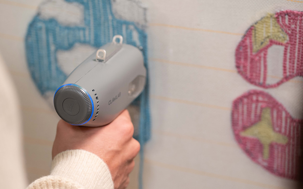 Hand holding the Clawlab Tufting Gun H1 and tufting with blue yarn.