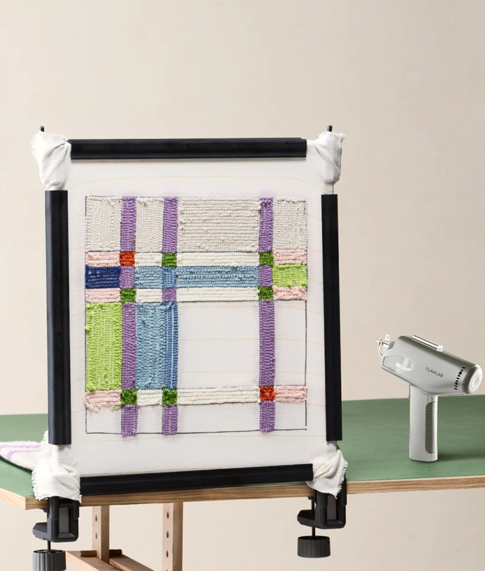 Clawlab H1 Lite tabletop tufting frame clamped to a desk with partially tufted colourful rug next to a grey tufting gun