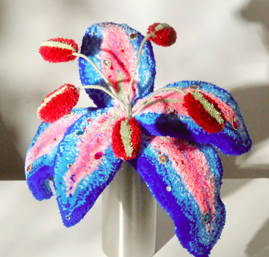 3D tufted lily sculpture made of blue, pink, and purple yarn decorated with rhinestones and red stamen.
