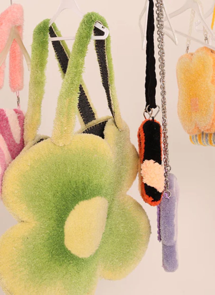 Plush green flower-shaped tufted tote bag hanging alongside handcrafted yarn accessories