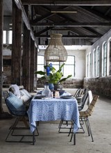 Superbe diner table setting, with a mix of chairs in iron, rattan and a wooden bench. Above the dining table a large naturel pendant lamp.