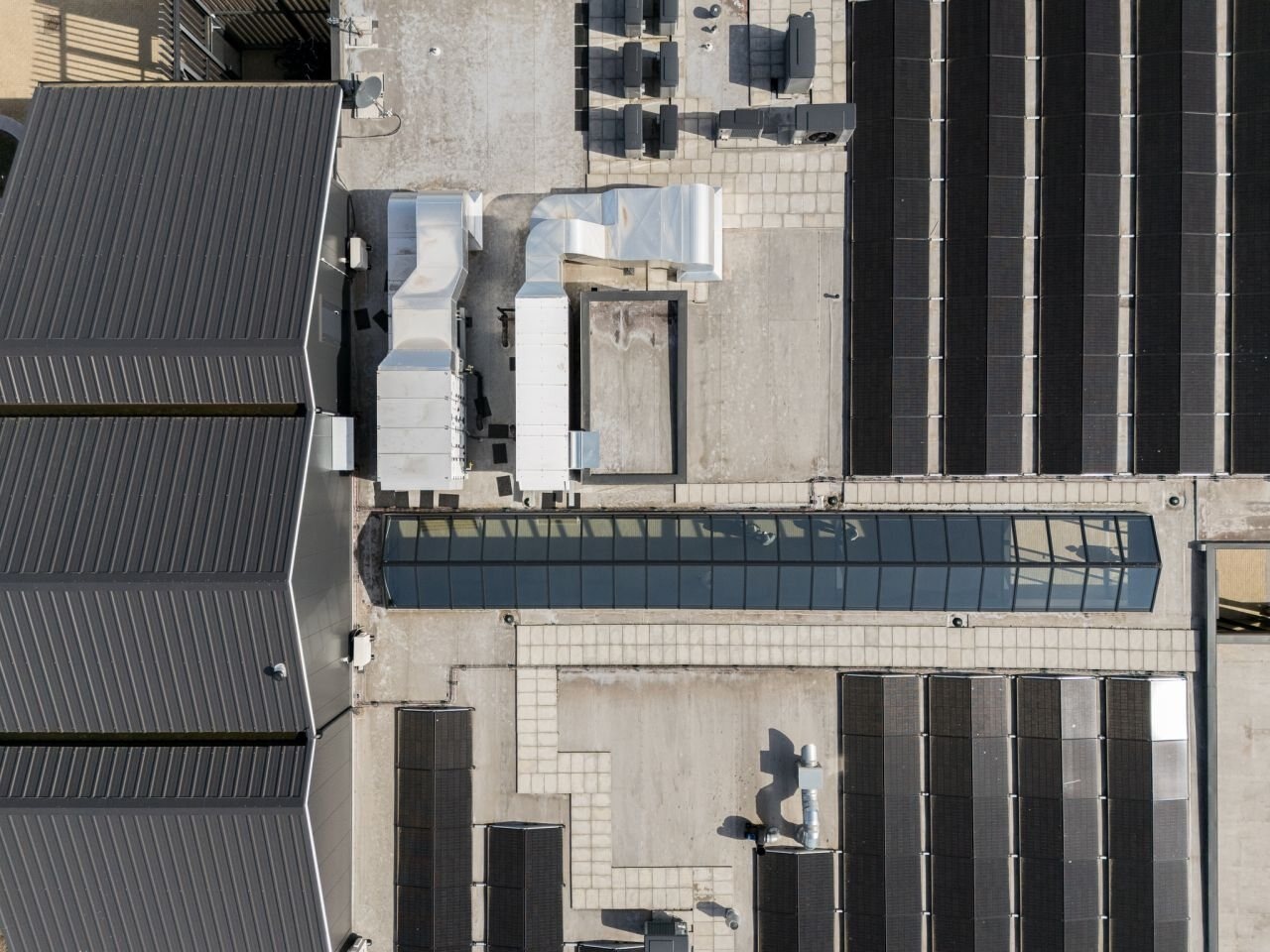 Lange lichtstraat tussen installaties en zonnepanelen op een utiliteitsdak