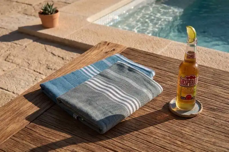 Ottomania XL hamamdoeken in oceaanblauw en dennengroen op houten tafel bij het zwembad