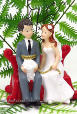 Bruidspaar zitten samen op een rode bank taarttopper
