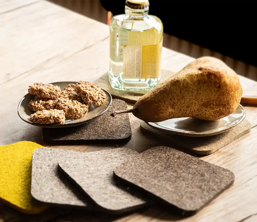 Felt coasters in beige, brown, and yellow featuring a small cookie bowl, a pear, and a small bottle